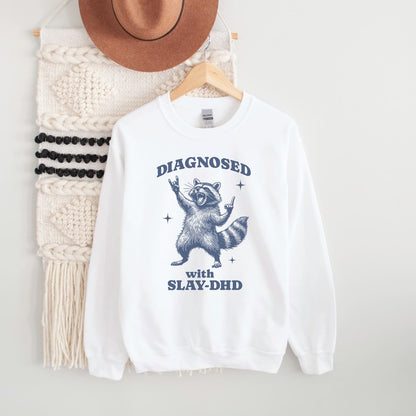 White adhd sweatshirt with raccoon graphic and text on a hanger with a hat and scarf.