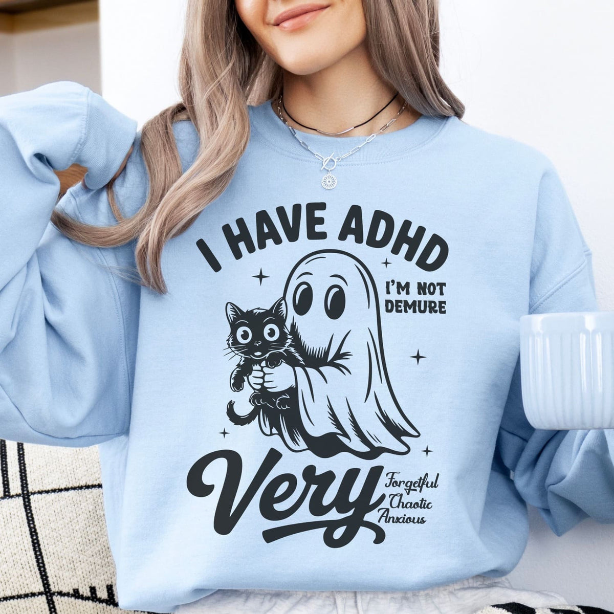 Person wearing a light blue spooky ADHD sweatshirt with a graphic and text, holding a mug