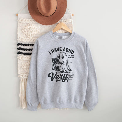 Gray sweatshirt with spooky ADHD design and text, placed on a white surface with a hat and bag in the background.