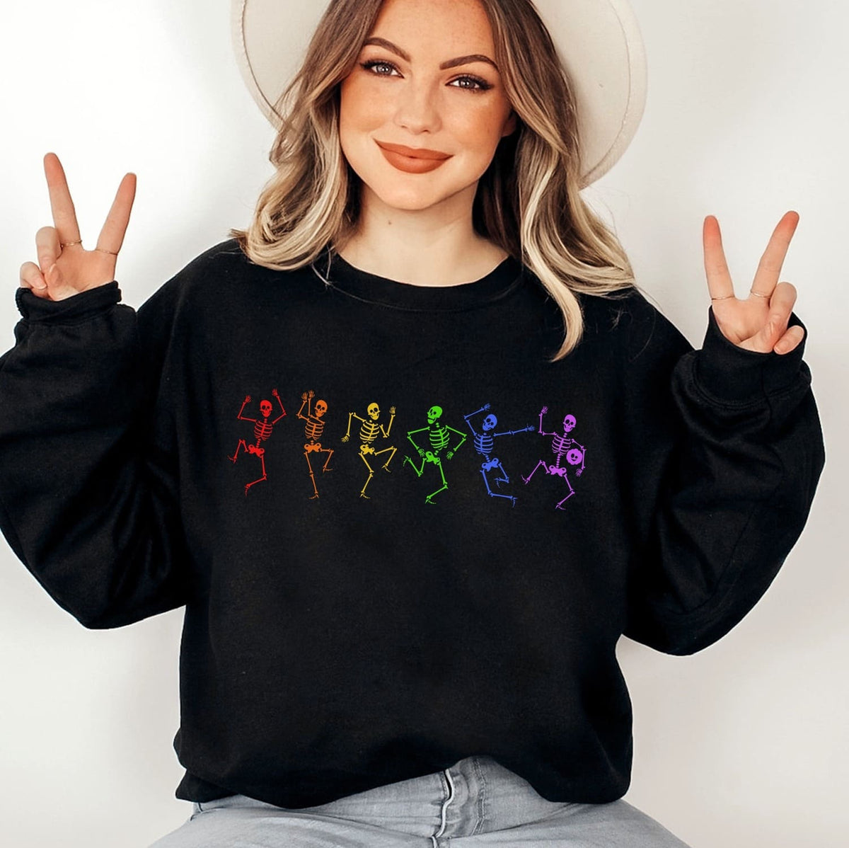 Person wearing a spooky sweatshirt with colorful pride skeleton designs and making peace signs.