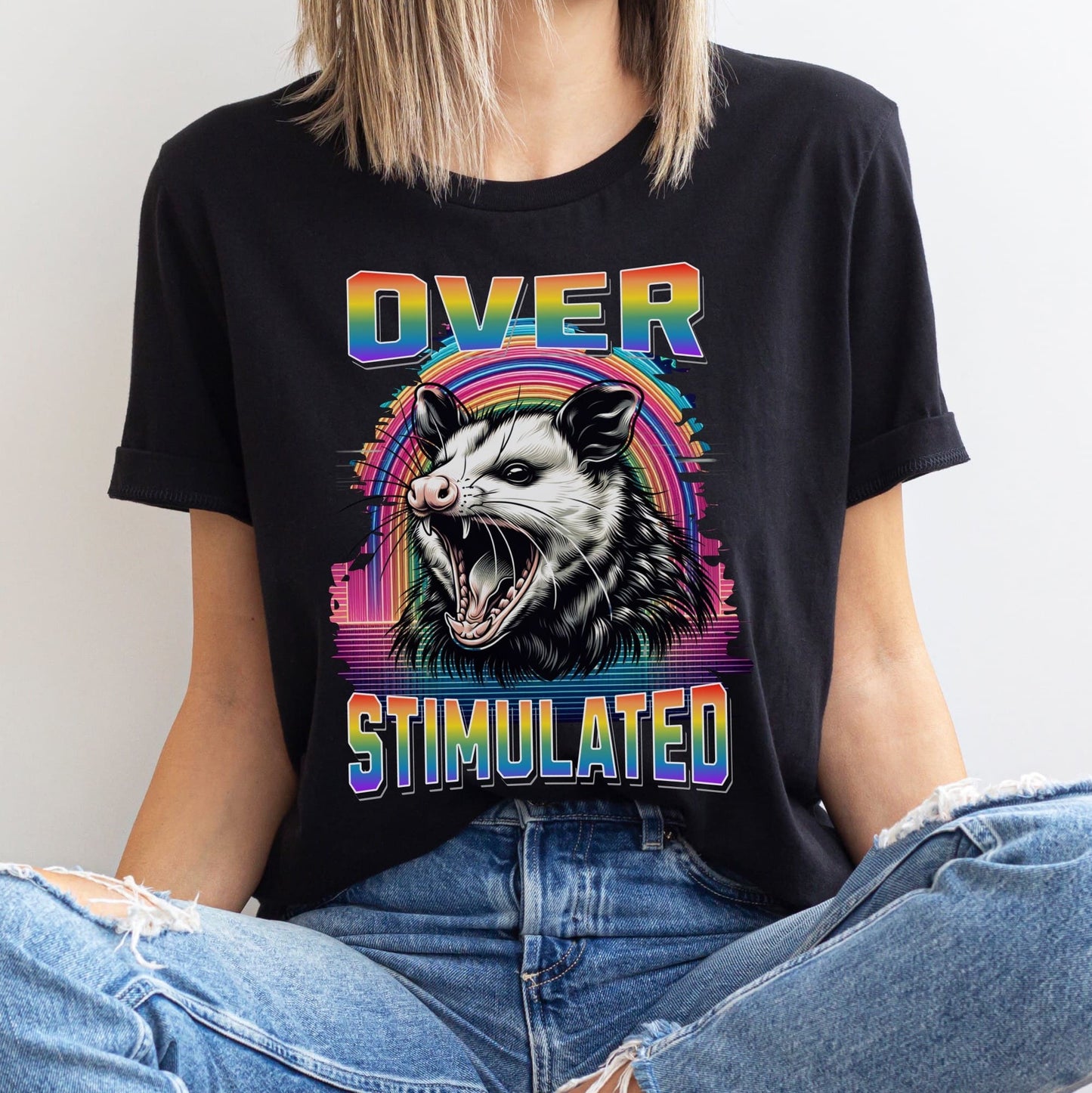 Person wearing a black t-shirt with a colorful graphic of an opossum and text 'OVERSTIMULATED': Subtle LGBT Overstimulated Shirt, Unhinged Opossum Gay Pride Tee, Queer Neurodivergent T-Shirt, Neurospicy Gift For Autistic ADHD AUDHD