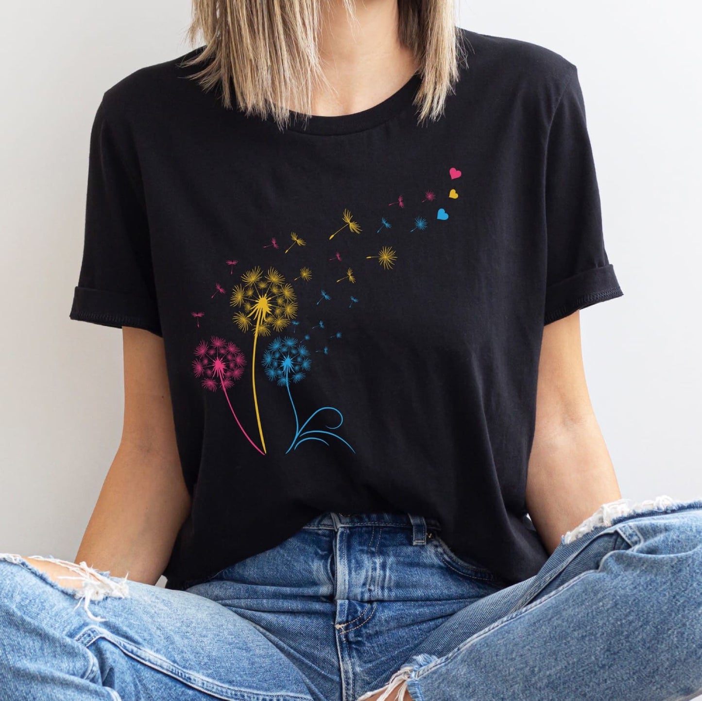 Person wearing a black t-shirt with colorful pan pride dandelion graphics and blue jeans.
