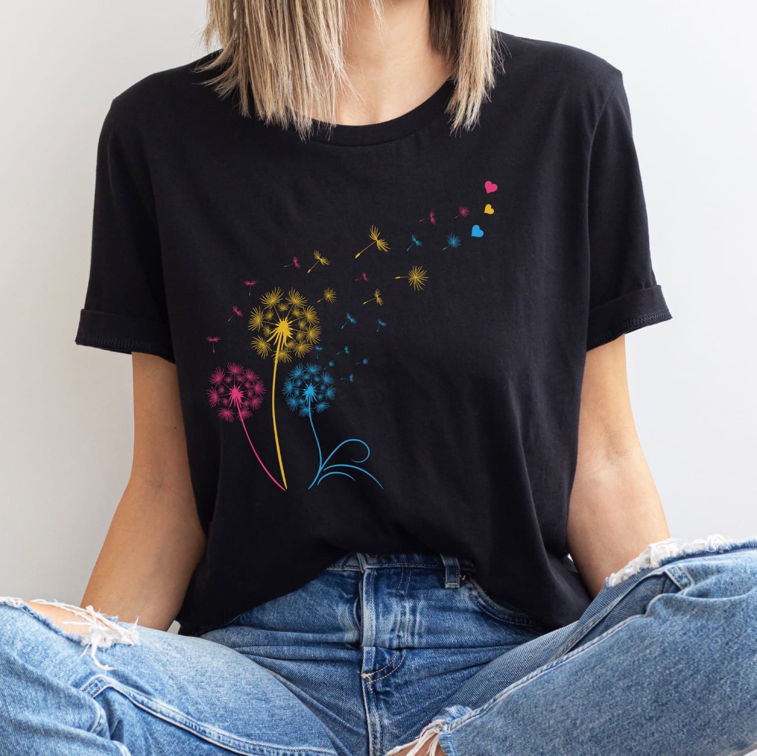 Person wearing a black t-shirt with colorful pan pride dandelion graphics and blue jeans.