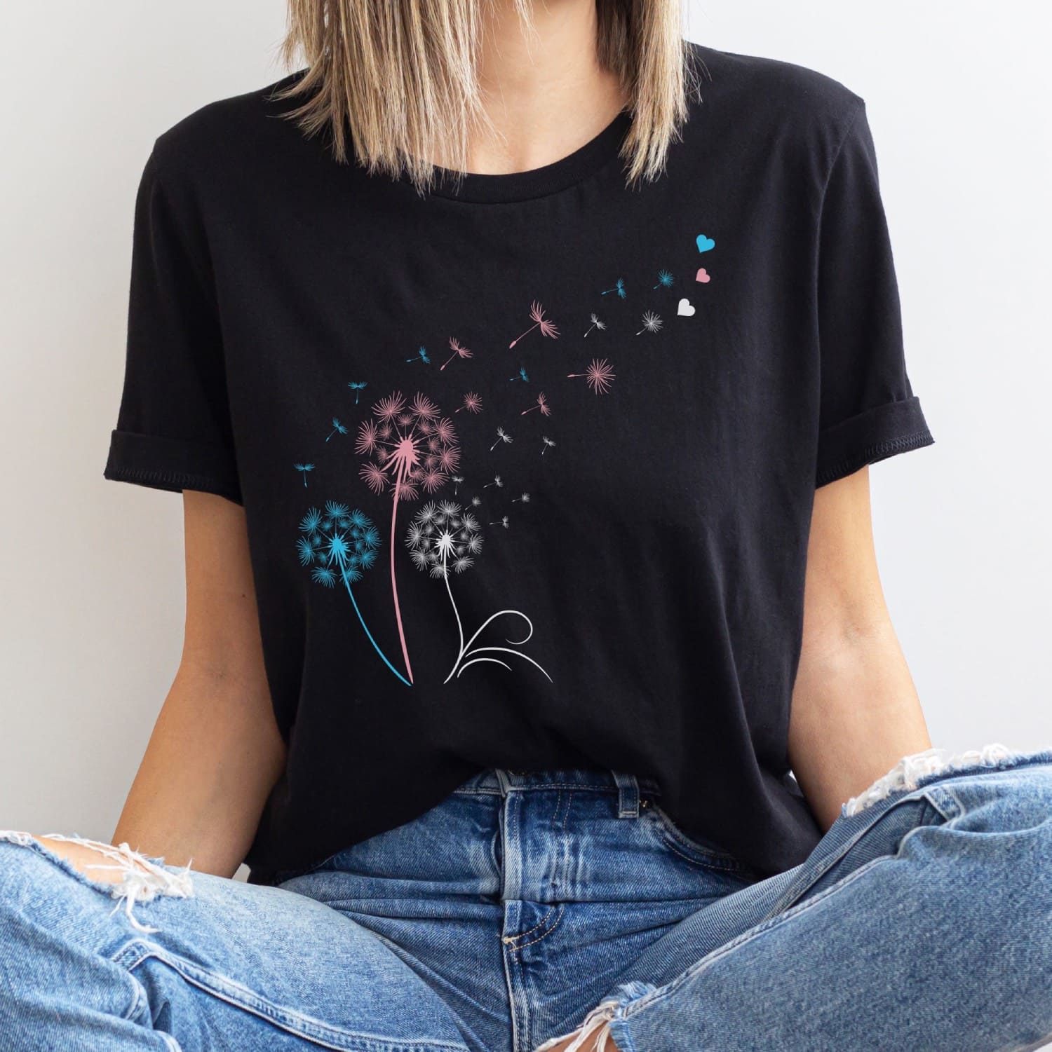 Person wearing a black t-shirt with colorful transgender dandelion graphic design.