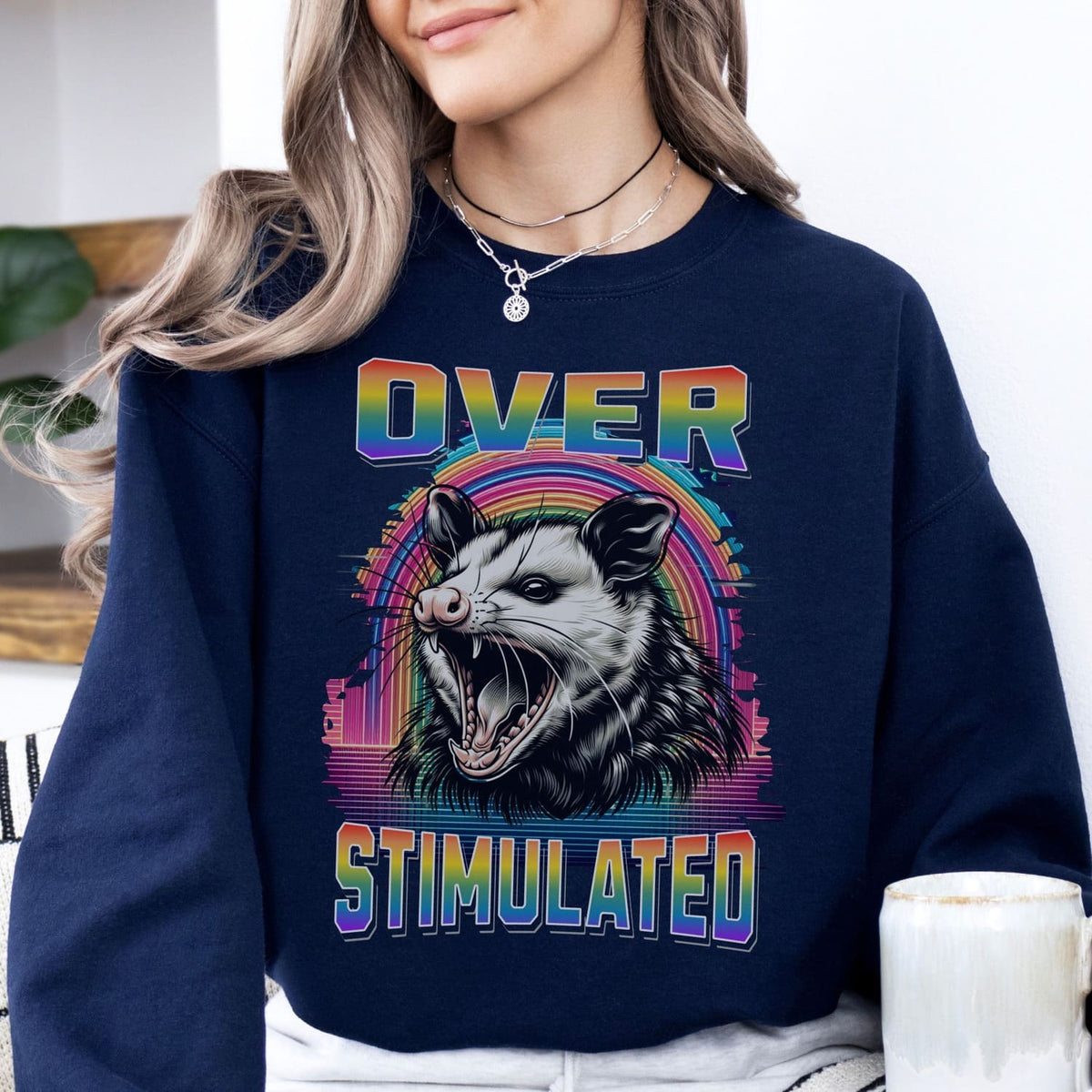 Person wearing a navy lgbt pride neurodivergent sweatshirt with an opossum graphic and 'Over Stimulated' text.