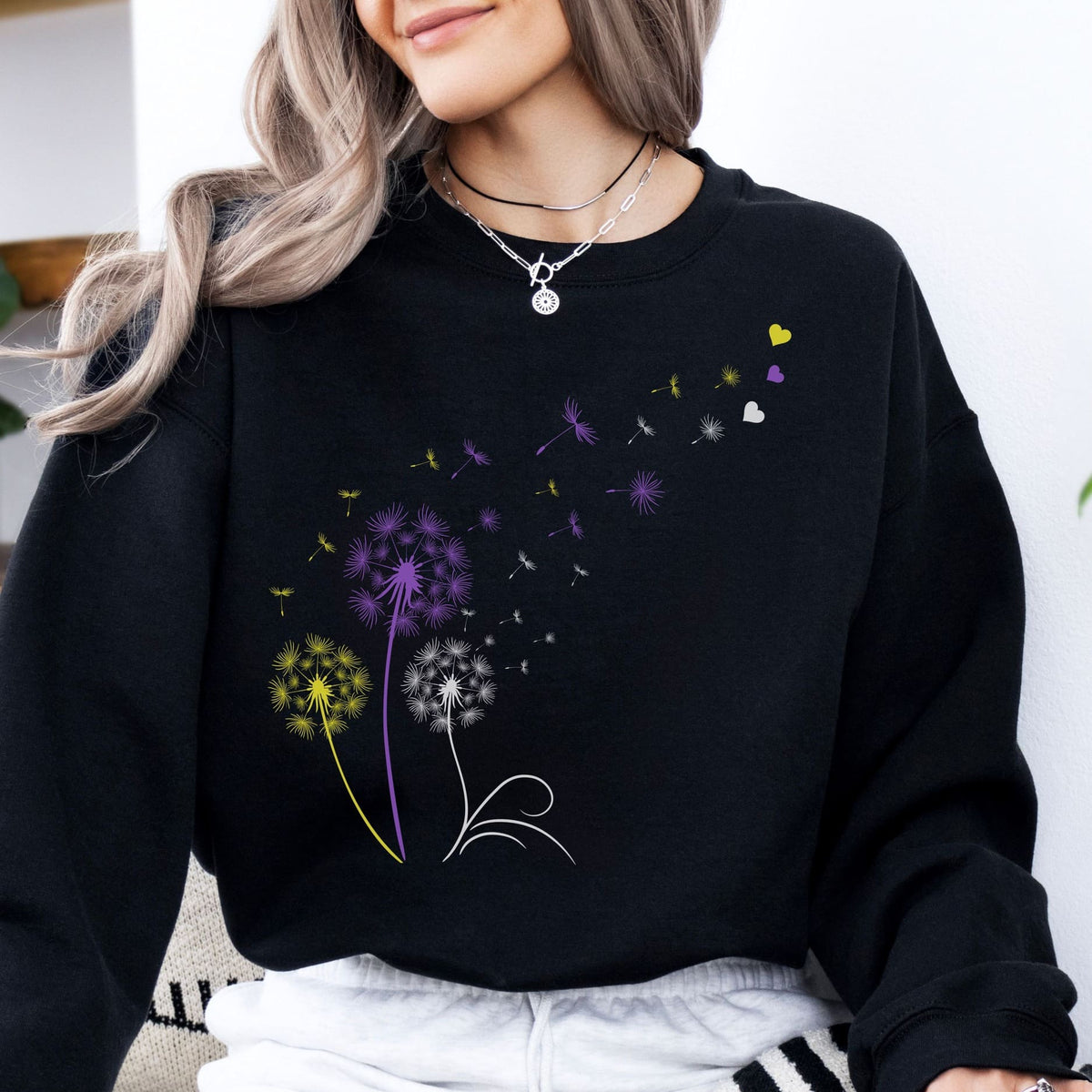 Person wearing a black enby pride sweatshirt with colorful dandelion designs.
