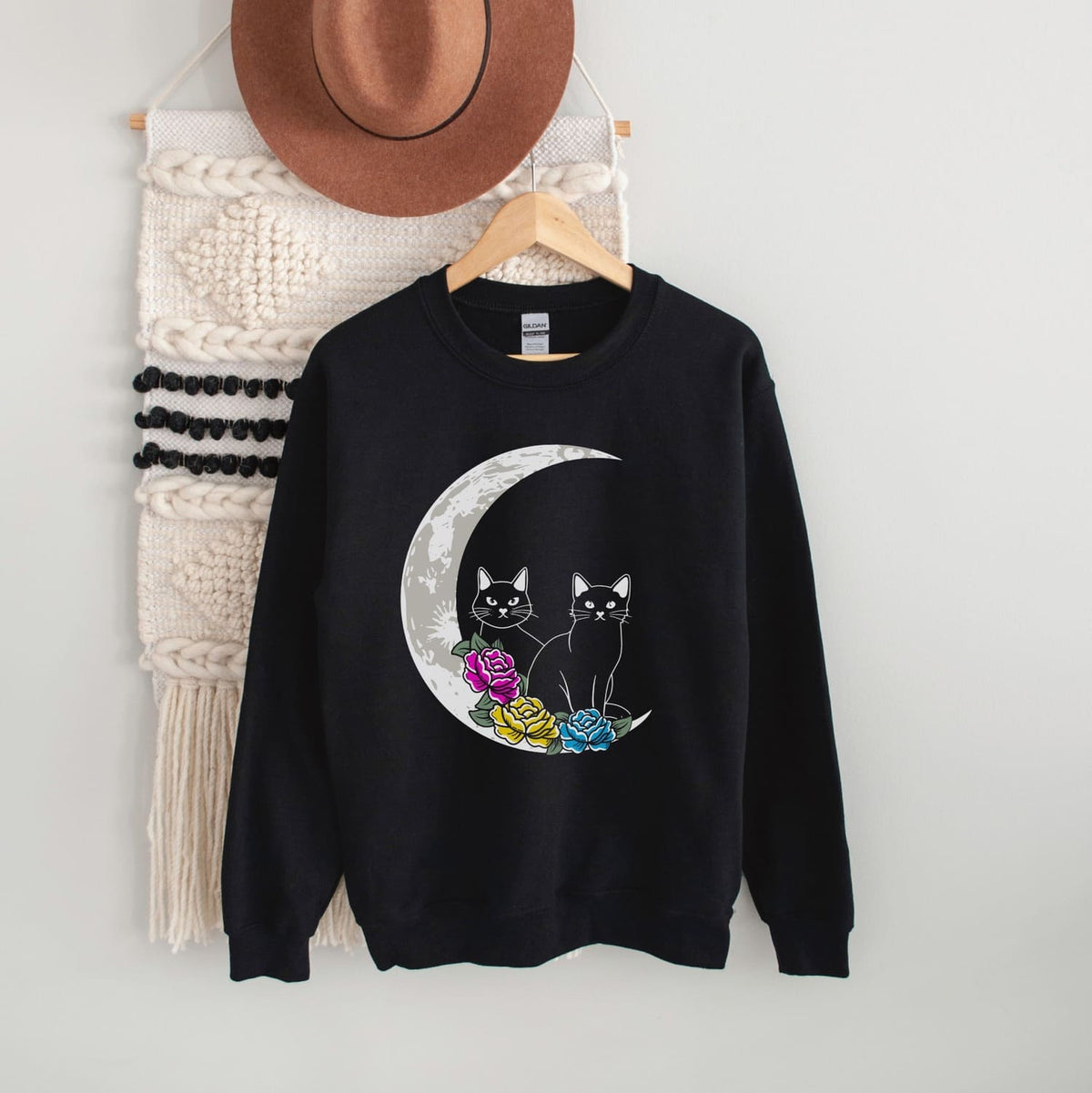 Pansexual sweatshirt with cat design on a hanger against a white wall.