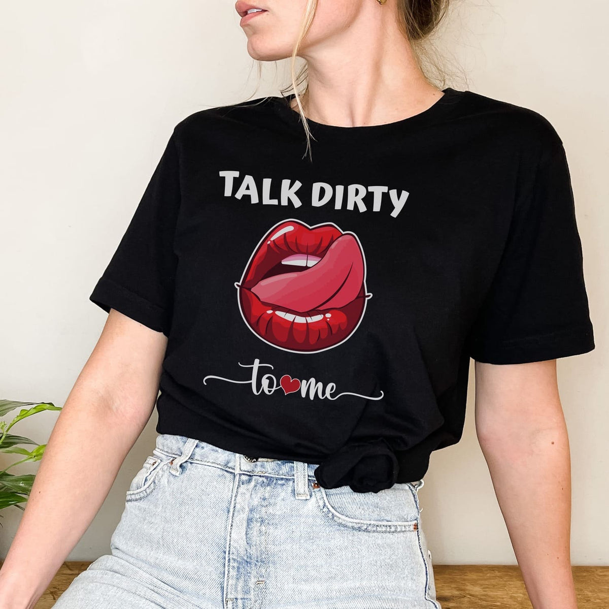 Person wearing a black t-shirt with a graphic of red lips and text 'Talk Dirty to Me' on a plain background.