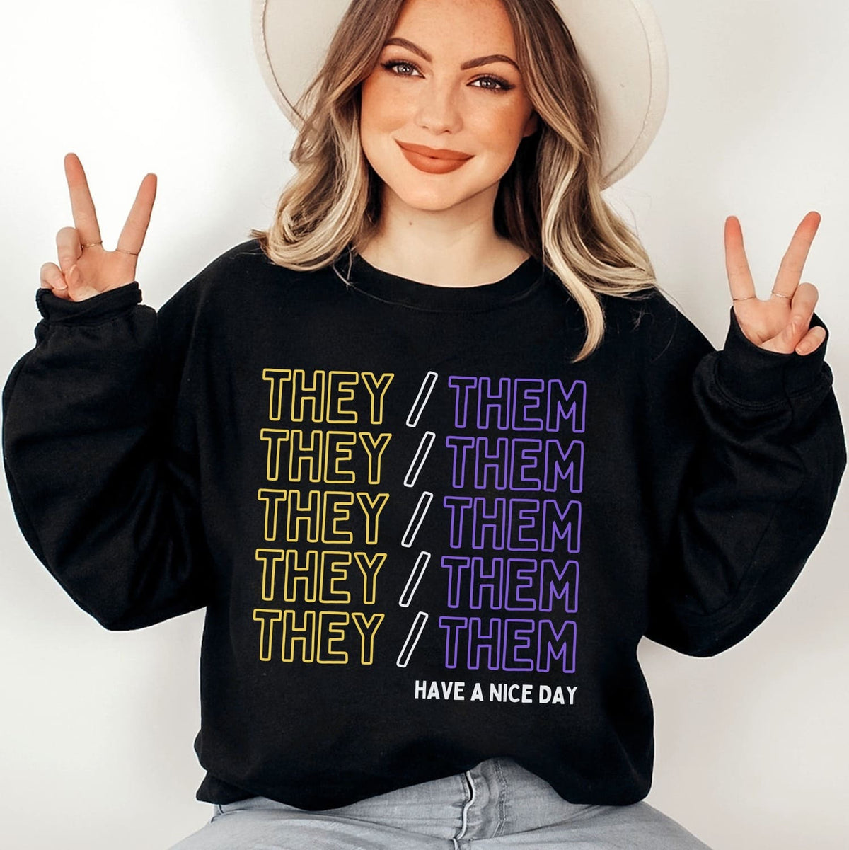 Enby Person wearing a black sweatshirt with 'THEY/ THEM' pronouns text and making peace signs.