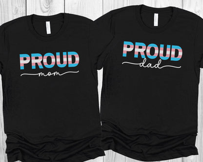 Two black transgender supporting t-shirts with 'PROUD mom' and 'PROUD dad' text on a wooden surface.