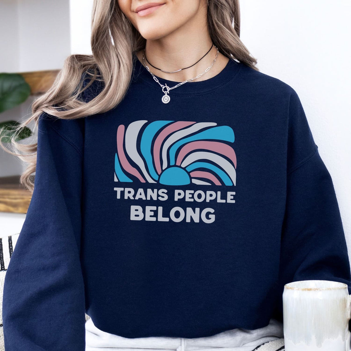 Person wearing a navy blue sweatshirt with a colorful design and 'Trans People Belong' text.