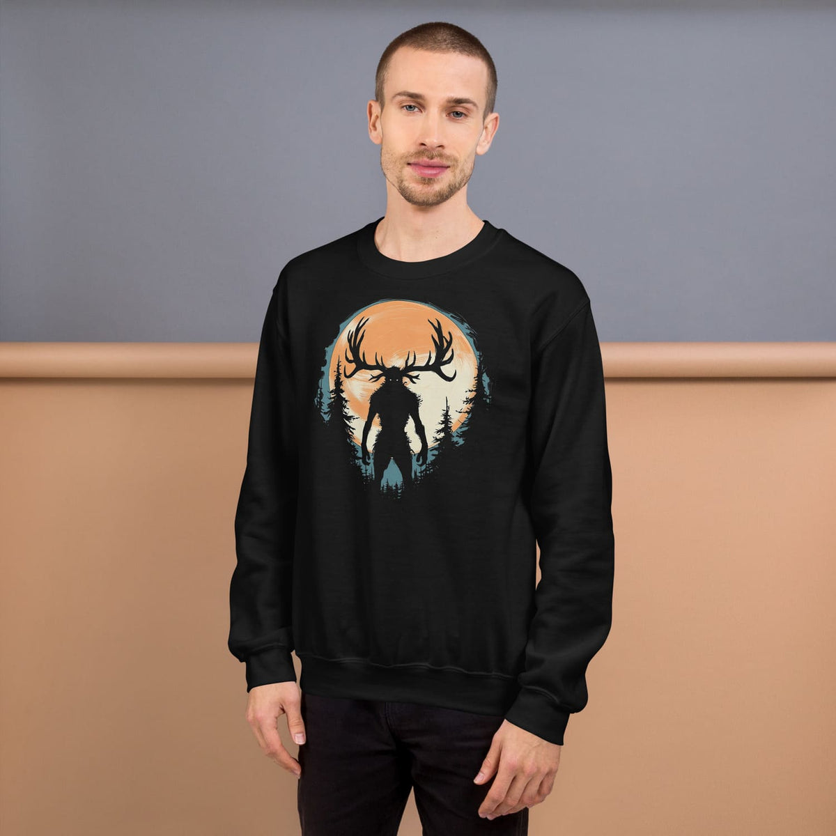 Man wearing a black sweatshirt with a graphic design of a forest and wendigo silhouette against an orange sky.