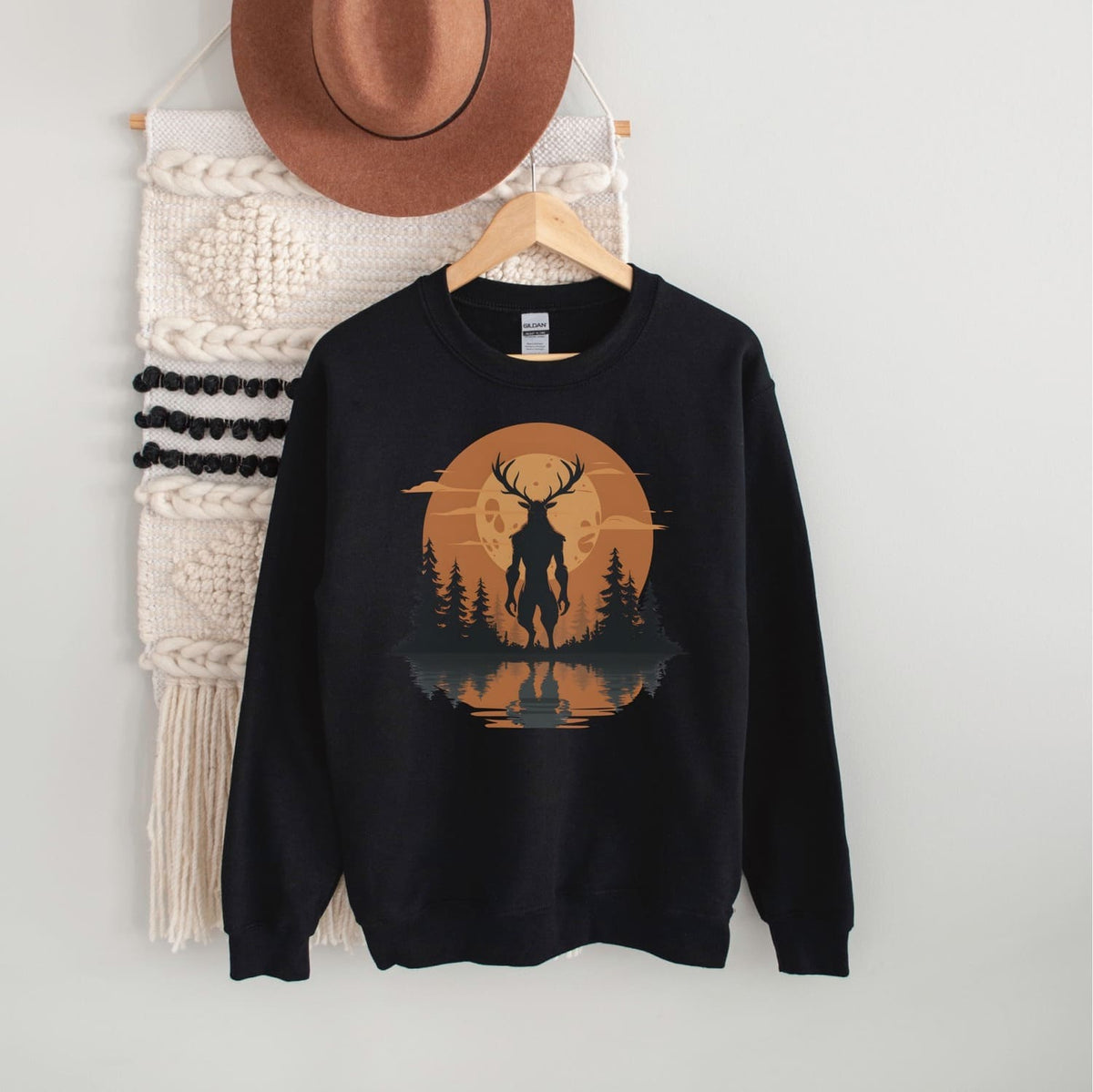 Black sweatshirt with a cryptid-themed design on a hanger against a white wall.