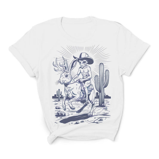 White t-shirt with a graphic design of an alien riding a jackalope, wearing a cowboy hat, in a desert landscape with cacti.