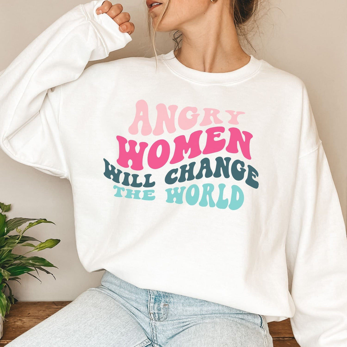Person wearing a white feminist sweatshirt with colorful text 'ANGRY WOMEN WILL CHANGE THE WORLD'.
