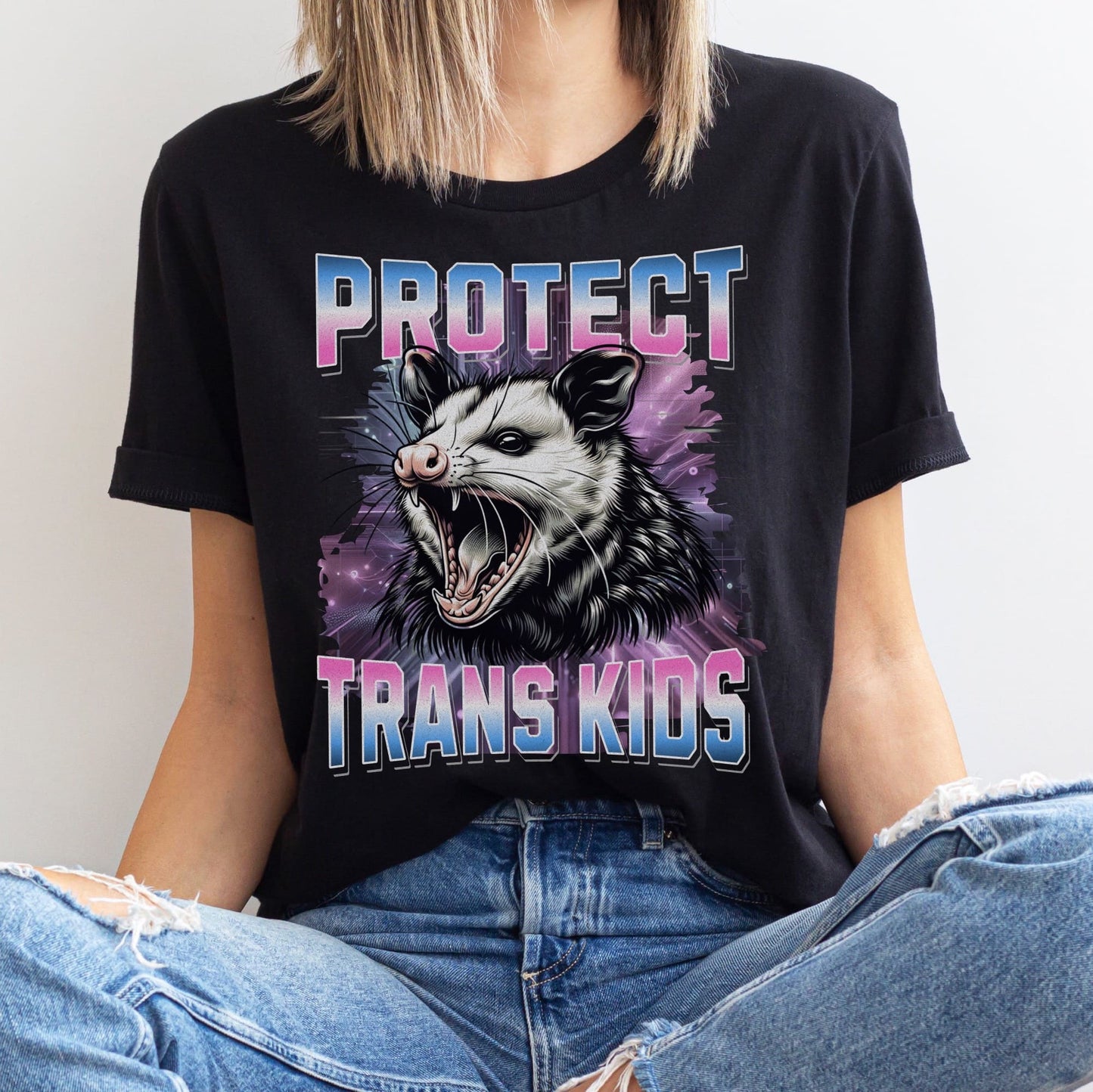 Person wearing a Y2K bootleg black transgender  t-shirt with an opossum graphic and text 'PROTECT TRANS KIDS' on a plain background