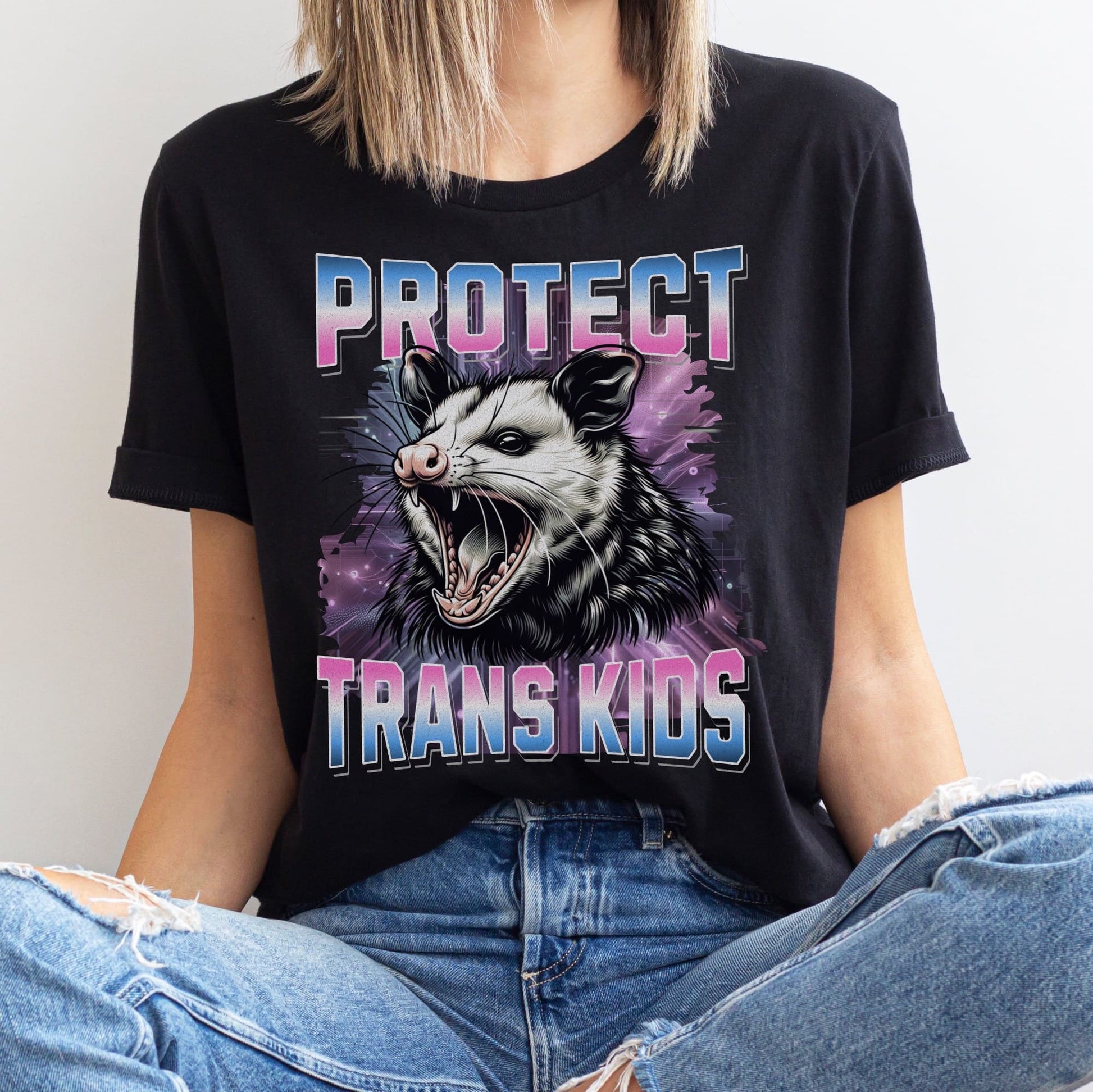 Person wearing a Y2K bootleg black transgender  t-shirt with an opossum graphic and text 'PROTECT TRANS KIDS' on a plain background