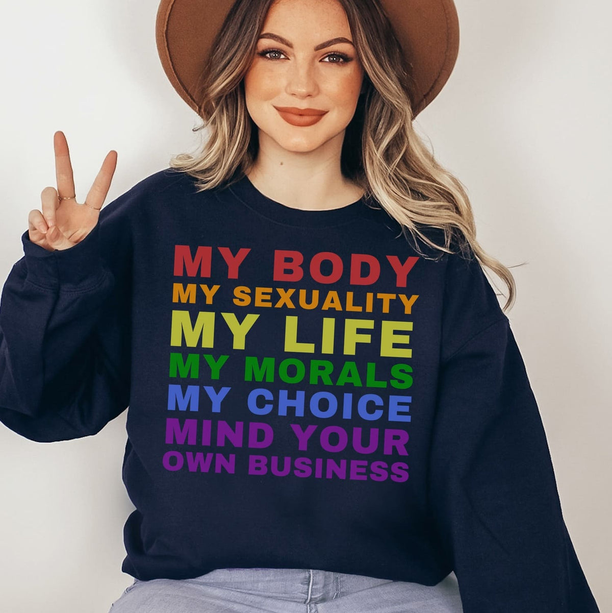 Person wearing a navy pride sweatshirt with colorful rainbow text, making a peace sign.