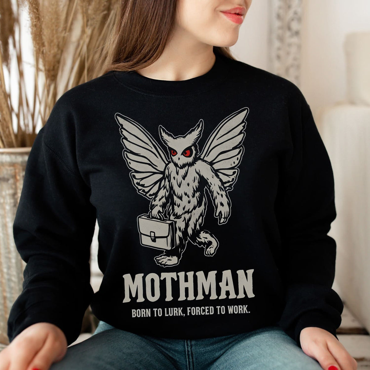 Person wearing a black sweatshirt with Mothman graphic and text