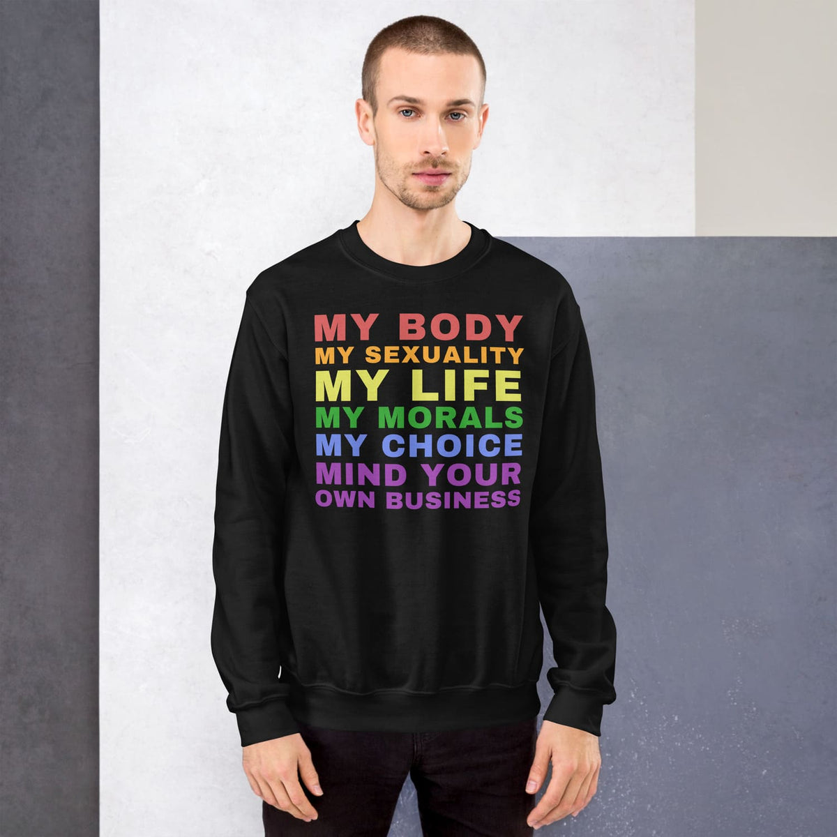 Man wearing a black LGBTQ sweatshirt with colorful rainbow text message on a gray background